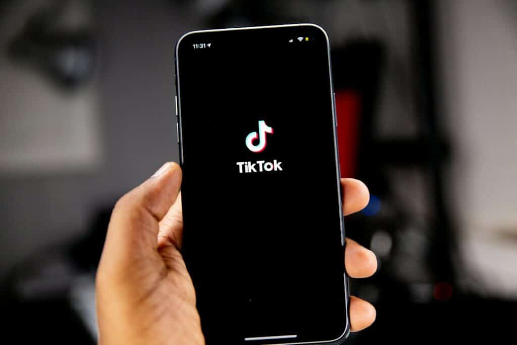 A hand holding a smartphone displaying the TikTok logo on a black screen